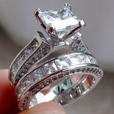 a close up of a person holding two wedding rings with princess cut diamonds on them