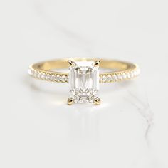 an emerald cut diamond engagement ring set in yellow gold with pave diamonds on the band