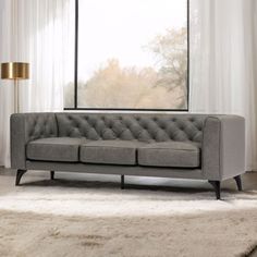 a gray couch sitting in front of a window next to a white rug on top of a wooden floor