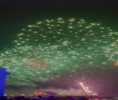 fireworks are lit up in the night sky above a cityscape with buildings and people watching