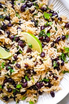 rice with black beans and cilantro is served on a white plate, garnished with lime wedges