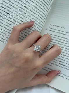 a woman's hand is holding an open book with a ring on top of it