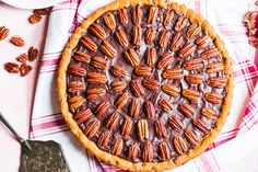 a chocolate pecan pie on a pink and white checkered table cloth next to a spoon