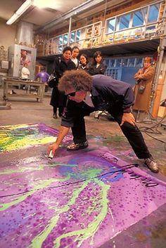 a group of people standing around a large piece of art painted on the ground with purple and green paint