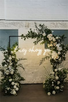 two white flowers and greenery are arranged in front of a neon sign that says, they're always you