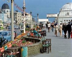 people walking down the street in front of shops and restaurants with cars parked on the side