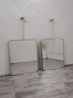 two mirrors sitting next to each other on top of a wooden floor in front of a white wall