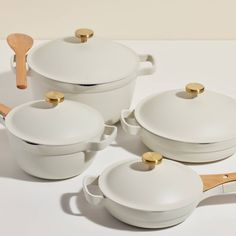 white ceramic pots and pans with wooden spoons on a white tablecloth background