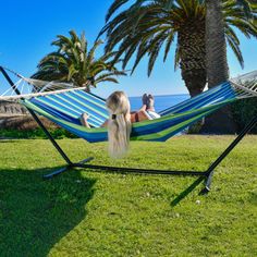 a woman laying in a hammock on the grass with palm trees behind her