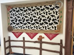 a cow themed wall hanging on the side of a building with a wooden fence in front of it