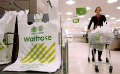 a woman pushing a shopping cart in a store with bags on the rack and an advertisement for waitrose