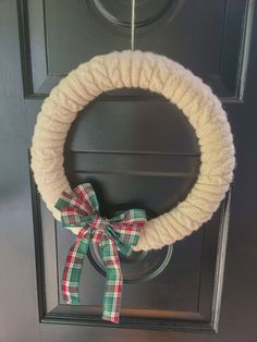 a yarn wreath hanging on the front door with a bow around it's neck