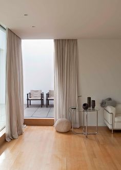 a living room filled with furniture next to a large glass window covered in white drapes