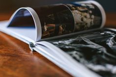 an open magazine on a wooden table with black and white photos in it's pages