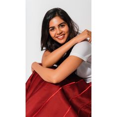 a smiling woman sitting on top of a red skirt with her arms folded over her chest