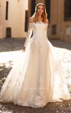 a woman in a white wedding dress standing on a cobblestone street wearing an off - the - shoulder lace and tulle gown