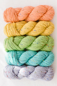 six skeins of yarn in different colors on a white surface with sprinkles