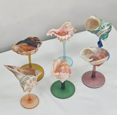 four different colored glass vases sitting on top of a white table covered in shells