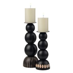 two candles sitting on top of each other next to some black balls and one white candle