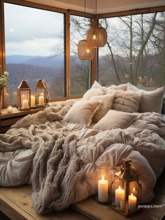 an unmade bed with candles and blankets on it in front of a large window