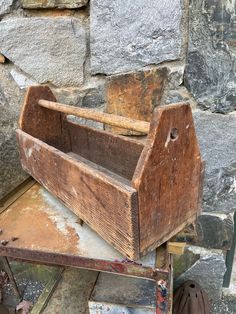 an old wooden toolbox sitting on top of a pile of metal parts next to a stone wall