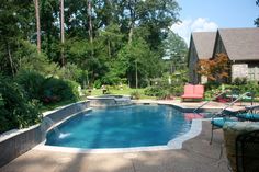 an empty swimming pool in the middle of a backyard with lounge chairs and trees around it