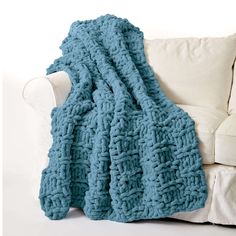 a blue crocheted blanket sitting on top of a couch next to a white pillow