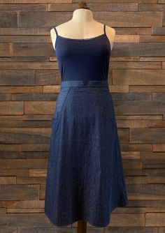 a mannequin wearing a blue dress on a wooden display stand in front of a brick wall