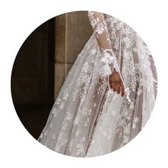 a woman in a white wedding dress with long sleeves and flowers on the skirt is holding her hand out