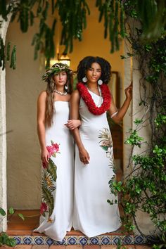 two women in white dresses standing next to each other with flowers on their heads and leis around their necks