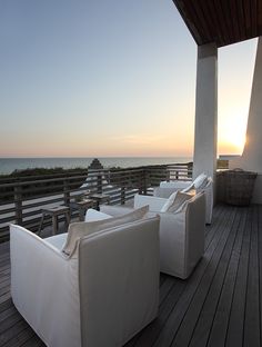 some white couches sitting on top of a wooden deck next to the ocean at sunset