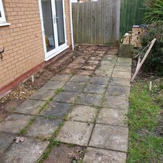 a brick walkway in front of a house with grass growing on the ground and bushes