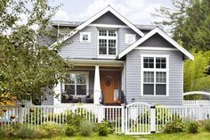 a gray house with white picket fence and trees