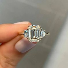 a woman holding an emerald and diamond ring in her left hand, with the center stone surrounded by smaller diamonds