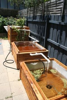 three wooden planters filled with dirt and water on the side of a fenced in area