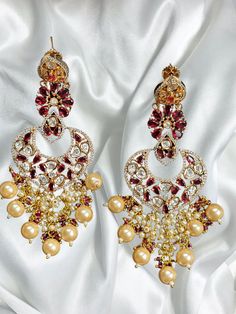 Introducing our stunning Indian Earrings, a mesmerizing blend of traditional craftsmanship and contemporary allure. These earrings showcase the timeless beauty of uncut polki and kundan, adorned with a captivating combination of pink and gold colors. Each earring is meticulously handcrafted by skilled artisans, paying homage to the rich heritage of Indian jewelry-making. The uncut polki stones, known for their raw and unrefined beauty, create a dazzling focal point. Set in a delicate framework of intricately designed gold-tone metal, these precious stones exude an aura of regality and sophistication. To further enhance their allure, the earrings feature intricate kundan work, a technique that involves setting glass stones to create a mosaic-like effect. The pink stones complement the uncut Luxury Earrings With 17 Jewels For Diwali, Luxury Drop Bridal Earrings For Diwali, Luxury Multicolor Chandbali Jhumkas, Luxury Bollywood Style Multicolor Jhumkas, Luxury Pink Fusion Earrings, Luxury Gold Chandelier Earrings With Meenakari, Pink Meenakari Chandelier Earrings Bollywood Style, Pink Meenakari Drop Earrings Danglers, Pink Meenakari Dangle Bridal Earrings