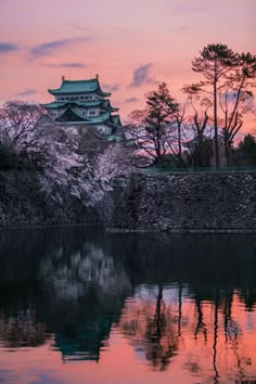 the castle is reflected in the still water at sunset with pink clouds and trees around it