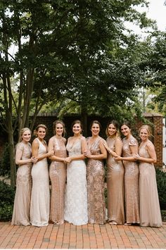 a group of women standing next to each other on a brick floored walkway with trees in the background