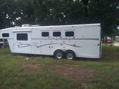 a horse trailer parked in the middle of a field with trees and grass behind it