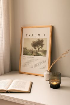 an open book sitting on top of a white shelf next to a candle and vase