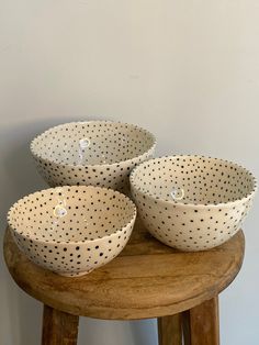 three white polka dot bowls sitting on top of a wooden stool next to a wall