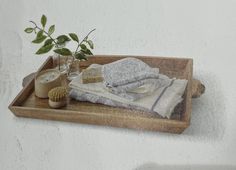 a wooden tray with towels, candles and a vase on it next to a plant