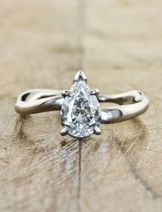 a pear shaped diamond ring sitting on top of a piece of wood