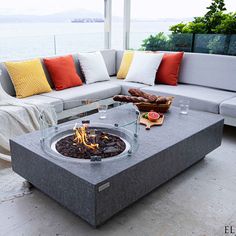 a fire pit sitting on top of a cement table next to a couch and pillows