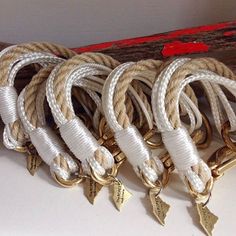 four gold and white rope bracelets with arrows on each end, sitting next to a red box