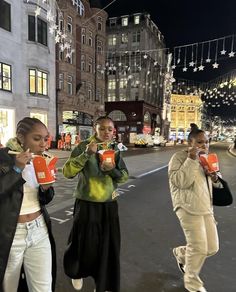 three women standing on the side of a city street at night, one holding up her cell phone to her ear