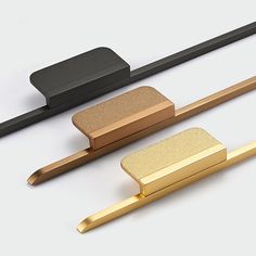 three different types of gold and black metal objects on a white surface, one with a square shaped object in the middle