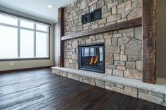 an empty room with a stone fireplace and wood flooring, along with large windows