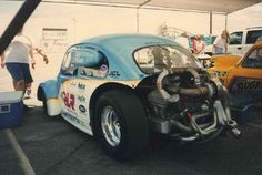 an old race car is parked in a lot with other cars and people around it