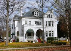 a large white house sitting on the side of a road with lots of trees in front of it